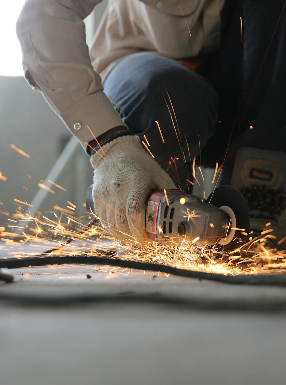 A skilled industrial worker uses a grinder creating a burst of sparks indoors.